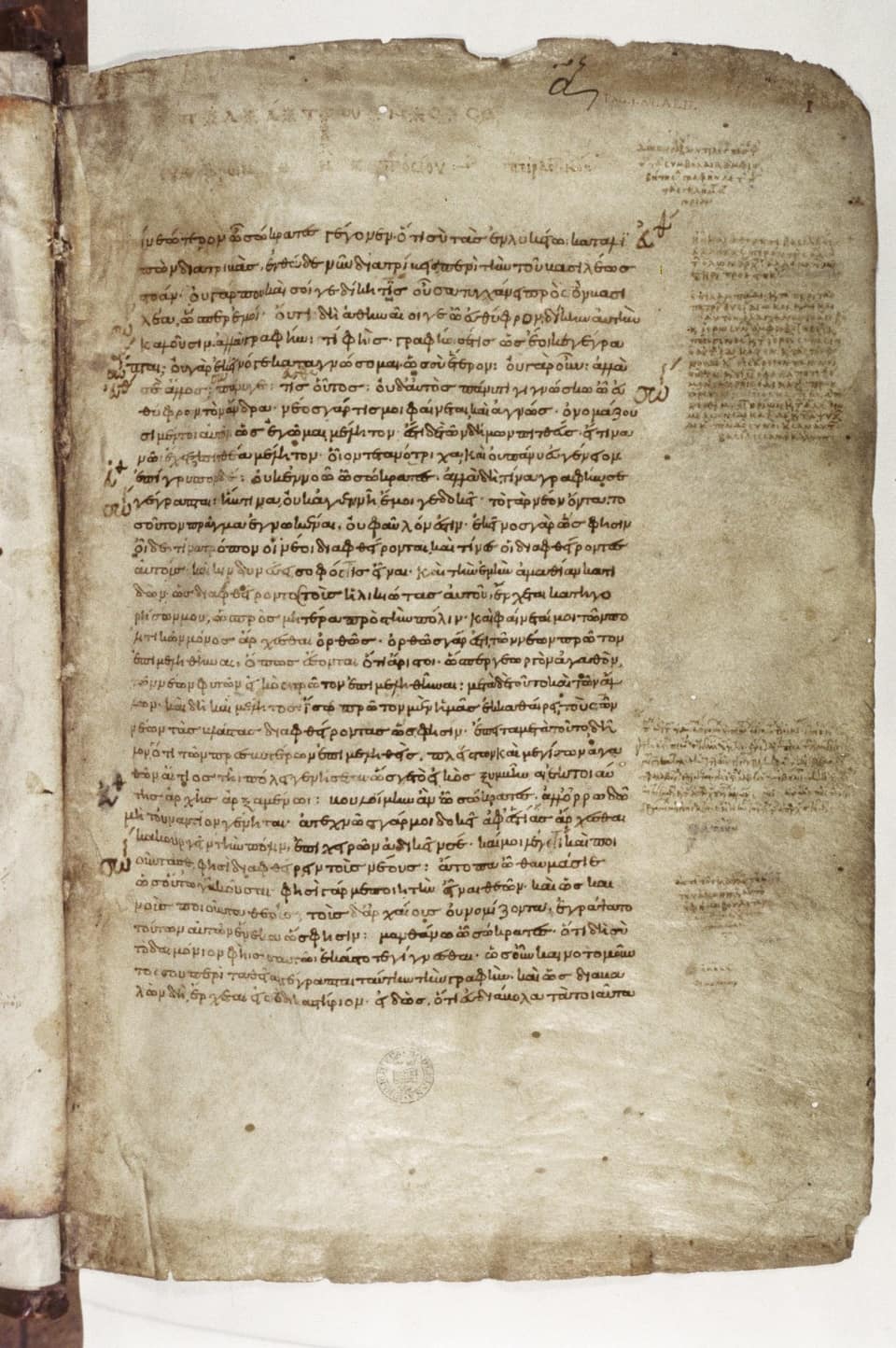 A page of yellowed parchment covered in two blocks of small, regular Greek minuscule script in brown ink, the main text in a wide column and fainter notes squeezed into the right margin, with the edge of the binding visible on the left.