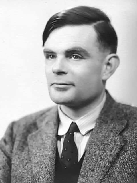 A black and white studio portrait of Alan Turing in 1951: a man in his late thirties with dark, neatly parted hair, in a tweed jacket, white shirt and dark tie, turned slightly to the left and looking past the camera with a faint smile.
