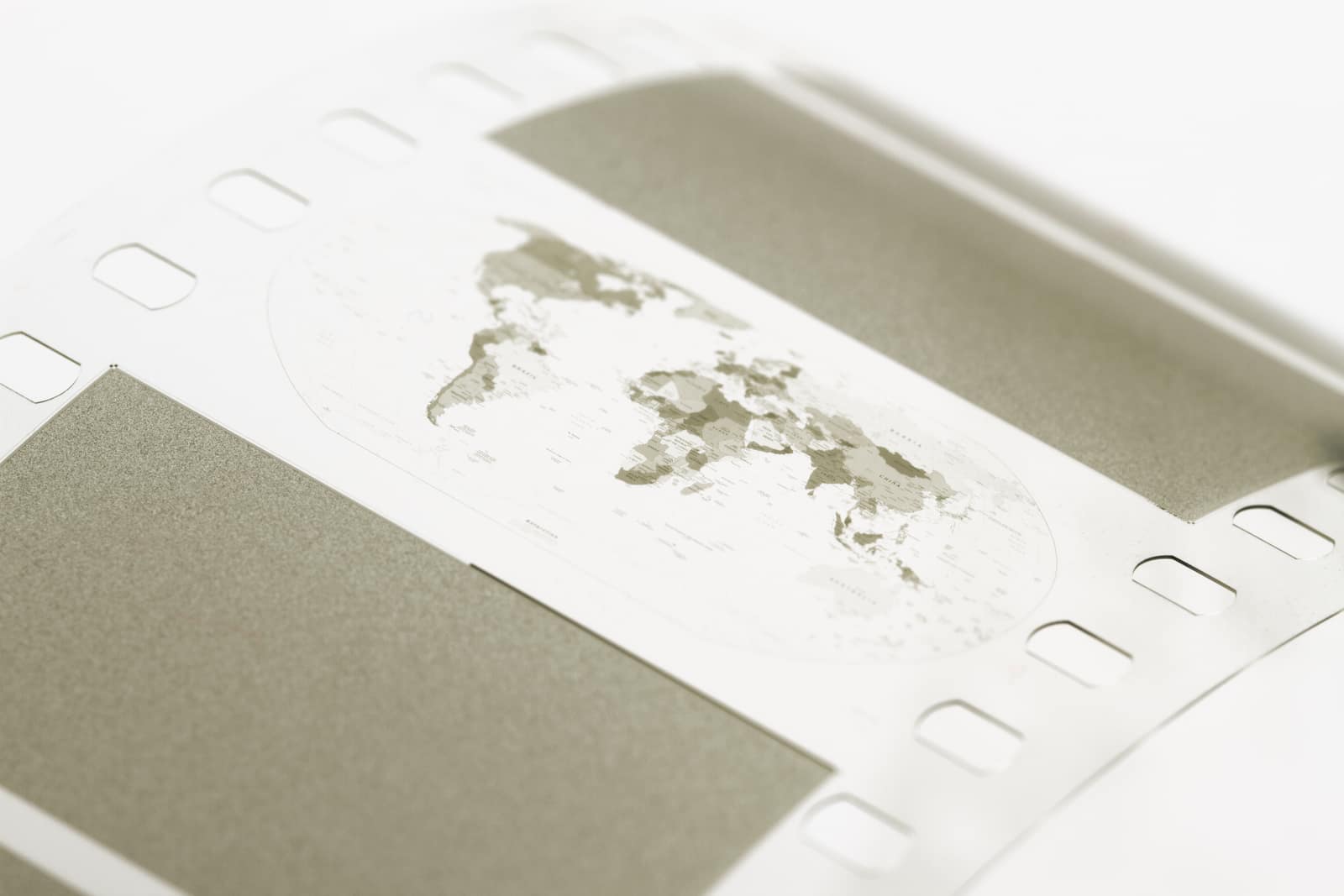 A close view of a strip of pale archival film with square perforations along its edges: at its centre a small printed map of the world in grey and olive, flanked by two dense grey rectangles of encoded data.