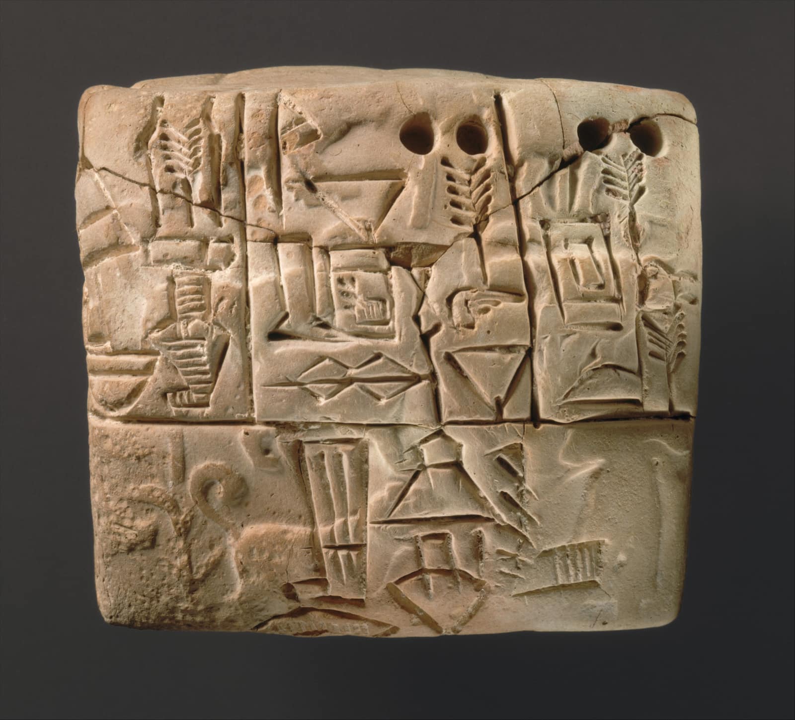 Une petite tablette épaisse d'argile claire, presque carrée, photographiée sur un fond gris sombre. Sa face est divisée en cases par des lignes incisées ; à l'intérieur, des signes imprimés et tracés dans l'argile : des épis, des trous ronds et des encoches en croissant pour les nombres, un vase, un triangle, une grille rectangulaire. En bas à gauche, un sceau déroulé a laissé une scène effacée où l'on devine un animal à la queue enroulée en spirale.