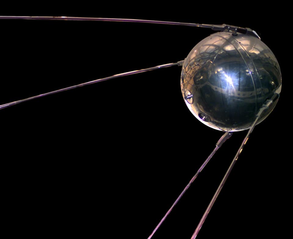 Sur fond noir, une sphère de métal poli, cerclée d'une jointure en son milieu, reflète la pièce alentour comme un miroir ; quatre longues antennes fines s'en échappent en oblique vers l'arrière, deux en haut et deux en bas.