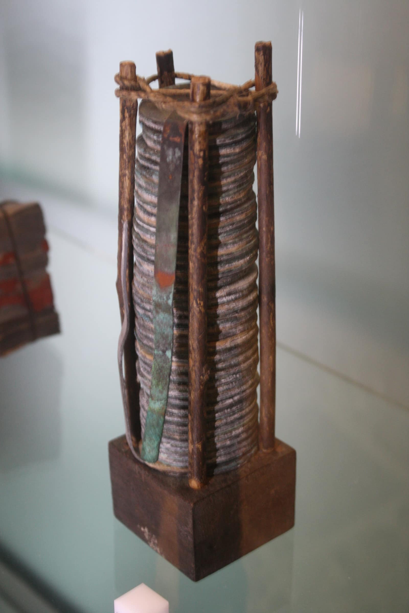 Une fine colonne de disques de métal gris, empilés à plat par dizaines, maintenue debout entre quatre baguettes de bois brut liées par une cordelette au sommet et fichées dans un socle de bois sombre ; une bande de cuivre verdie par la corrosion descend le long de la pile. Elle est exposée dans une vitrine du Tempio Voltiano, à Côme.