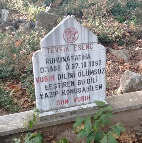 Une petite stèle blanche au sommet pointu se dresse dans un cimetière de village envahi d'herbes et de feuilles mortes. Sous un médaillon calligraphié rouge, des capitales noires et rouges, en turc, donnent le nom de Tevfik Esenç, les dates 1906 et 07.10.1992, et une épitaphe qui le dit le dernier Oubykh capable d'écrire et de parler la langue oubykh.