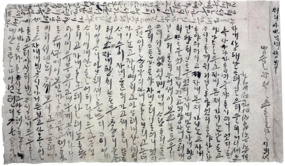 Une large feuille de papier clair et froissé, tachée et usée sur les bords, couverte de colonnes serrées de hangeul tracées au pinceau à l'encre noire ; les colonnes se lisent de droite à gauche, et, parvenue au bord gauche, l'autrice a tourné la feuille pour remplir la marge du haut de lignes plus petites écrites dans l'autre sens.